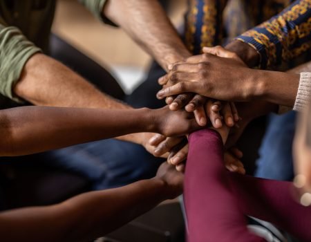 Cropped close of diverse businesspeople putting their hands on top of each other wearing casual clothes and african patterns.
